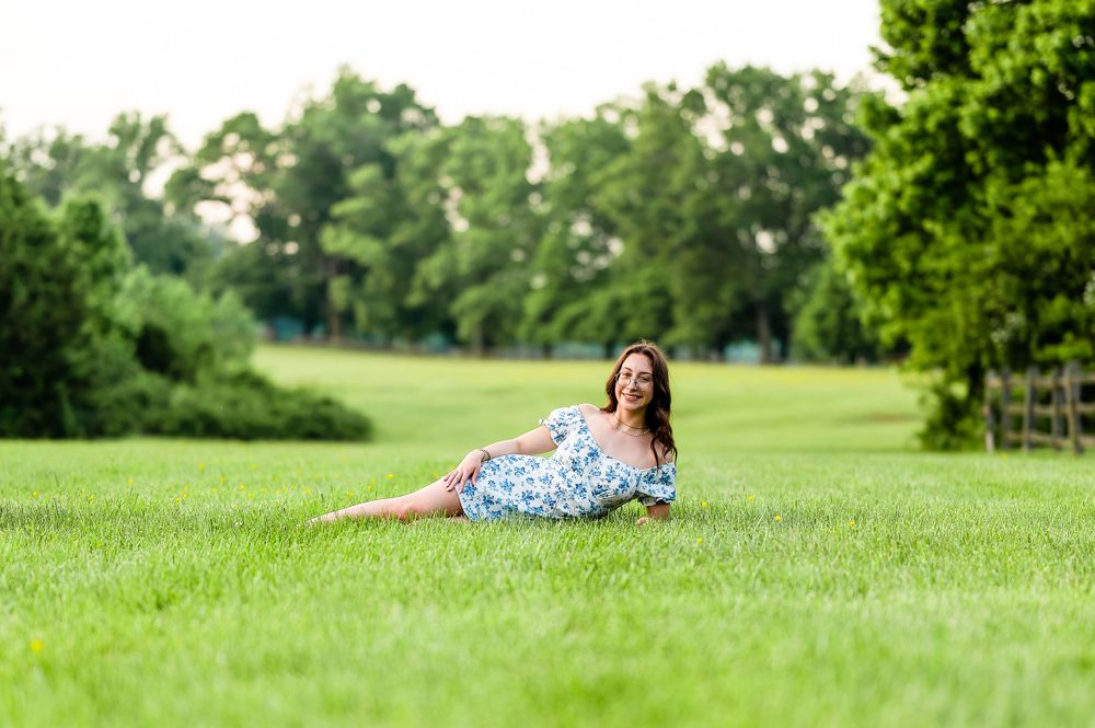 A person in a floral dress relaxes on lush green grass in a sunlit park.