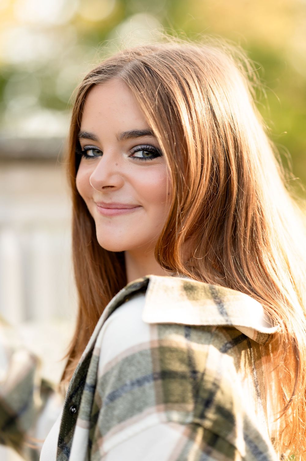 Portrait with warm lighting showing someone in a plaid flannel smiling at the camera.