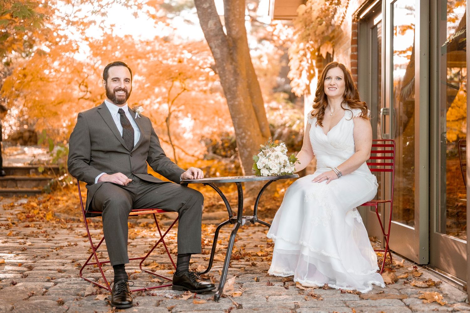 Autumn wedding portrait on rustic patio with orange fall foliage in background.