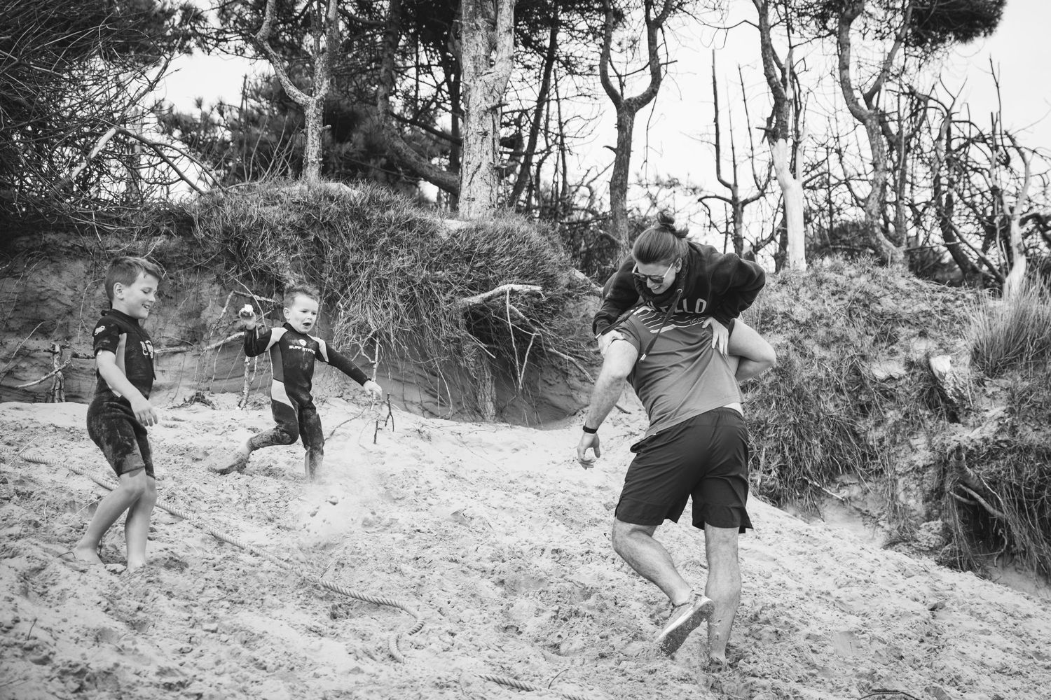 People jumping and playing on sandy dunes among trees in black and white.