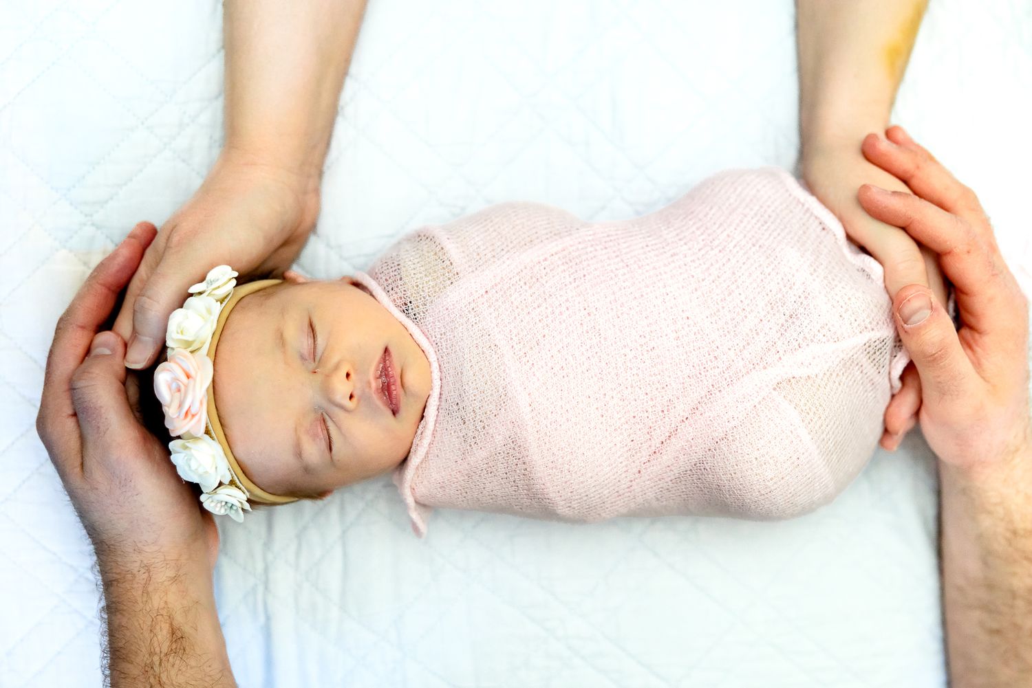 Baby girl lies sleeping with her parents hands around her during lifestyle newborn photos in Colorado Springs.