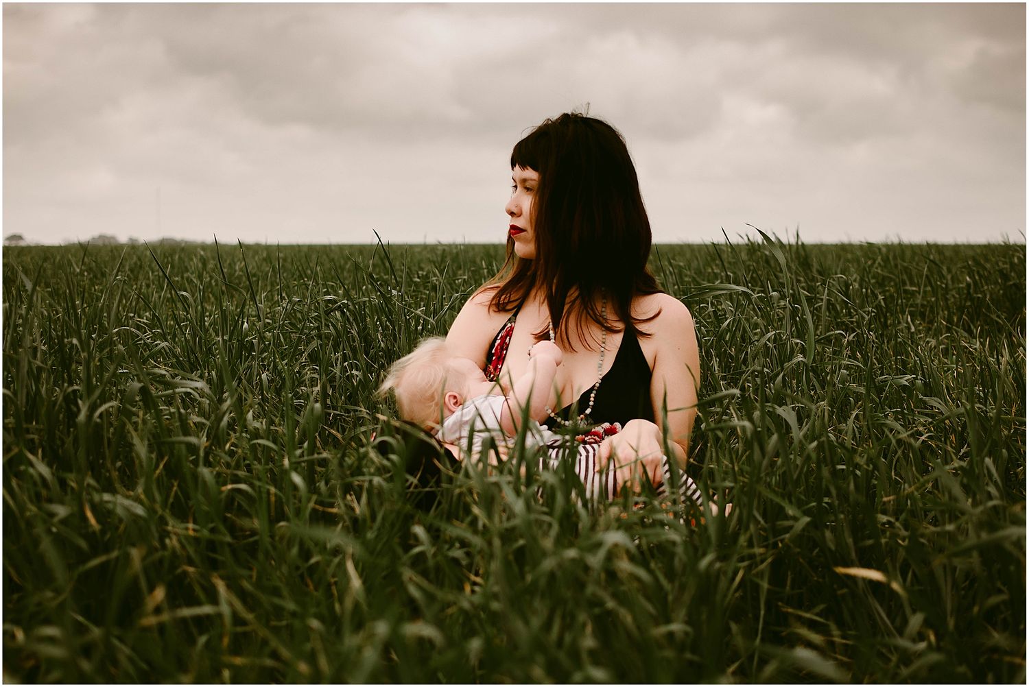 Moody portrait taken in tall grass field under cloudy sky.