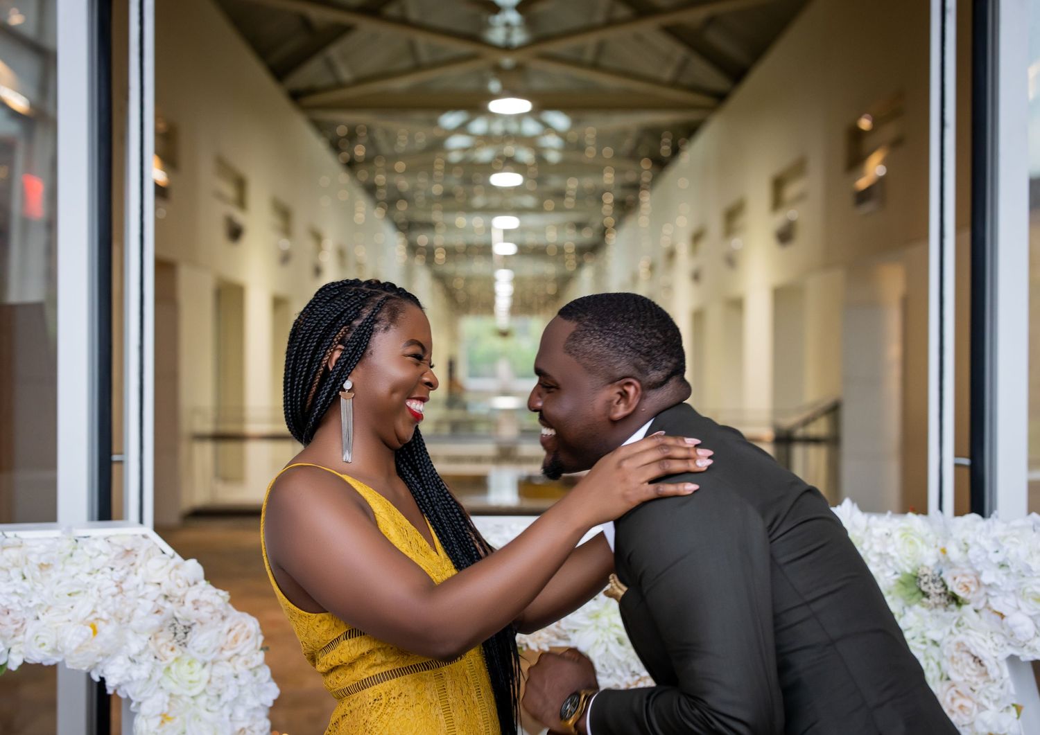 A joyful couple laughs together in an elegant hallway decorated with floral arrangements.