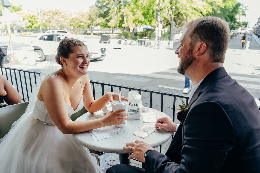 A couple smiles with each other seated at a Cafe du Monde table.