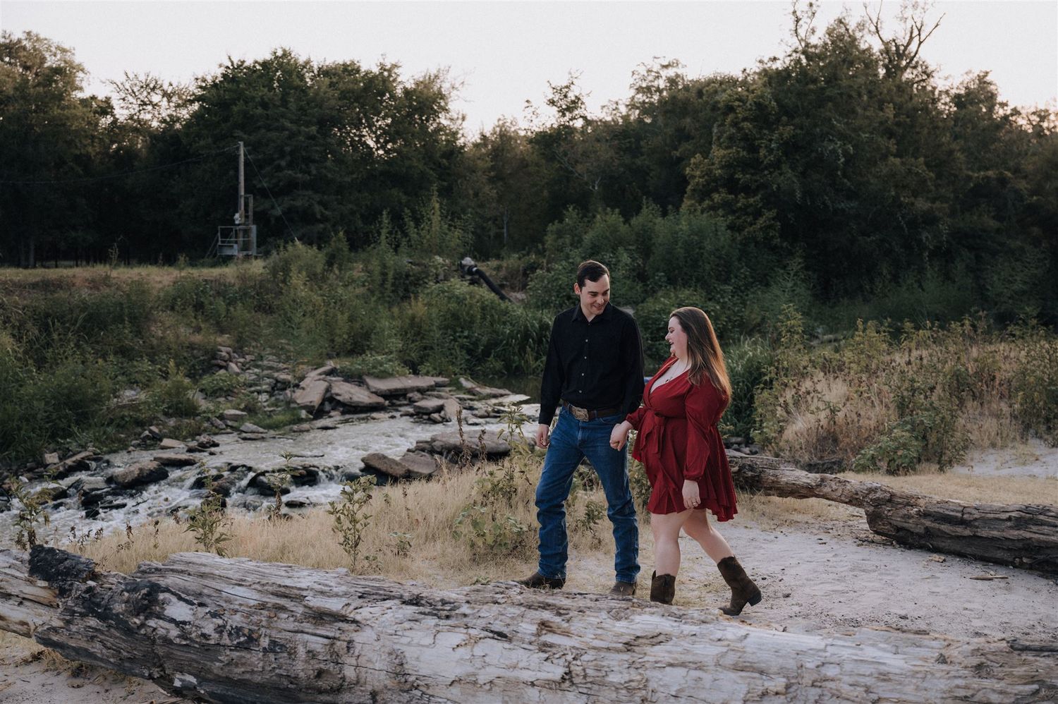 A couple walks together on rocky terrain near a stream at sunset.