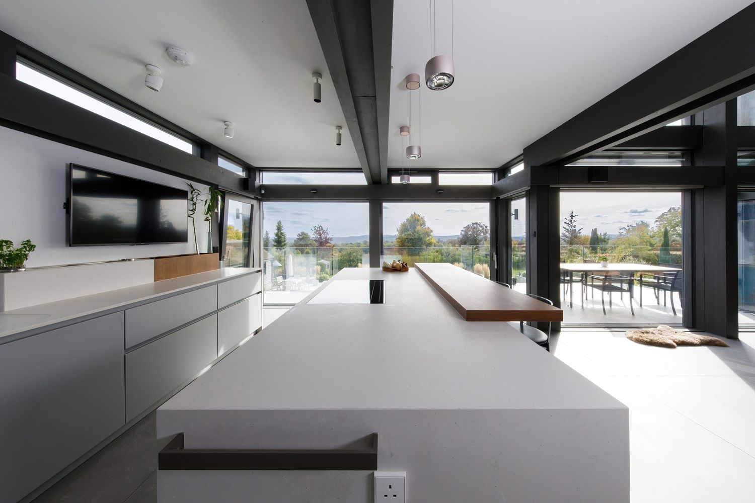 Bright modern kitchen with expansive windows, white countertops, and structural black ceiling beams taken during an interiors photoshoot.