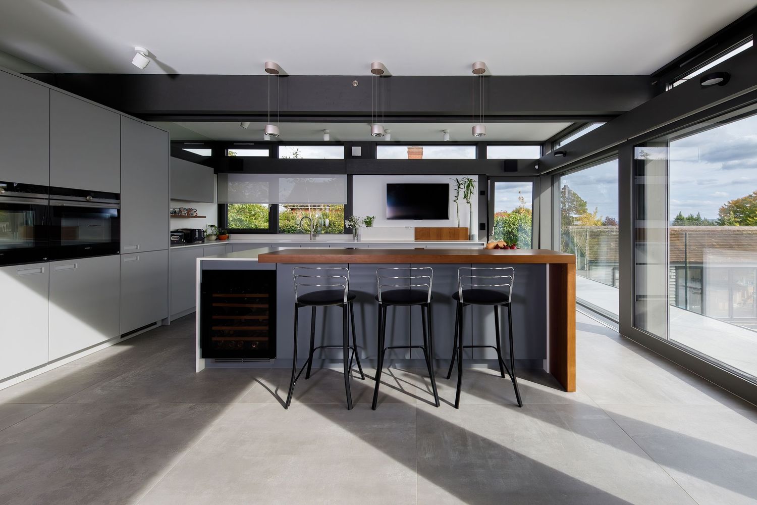 Modern kitchen island with black bar stools and wood accents featuring floor-to-ceiling windows with outdoor views.