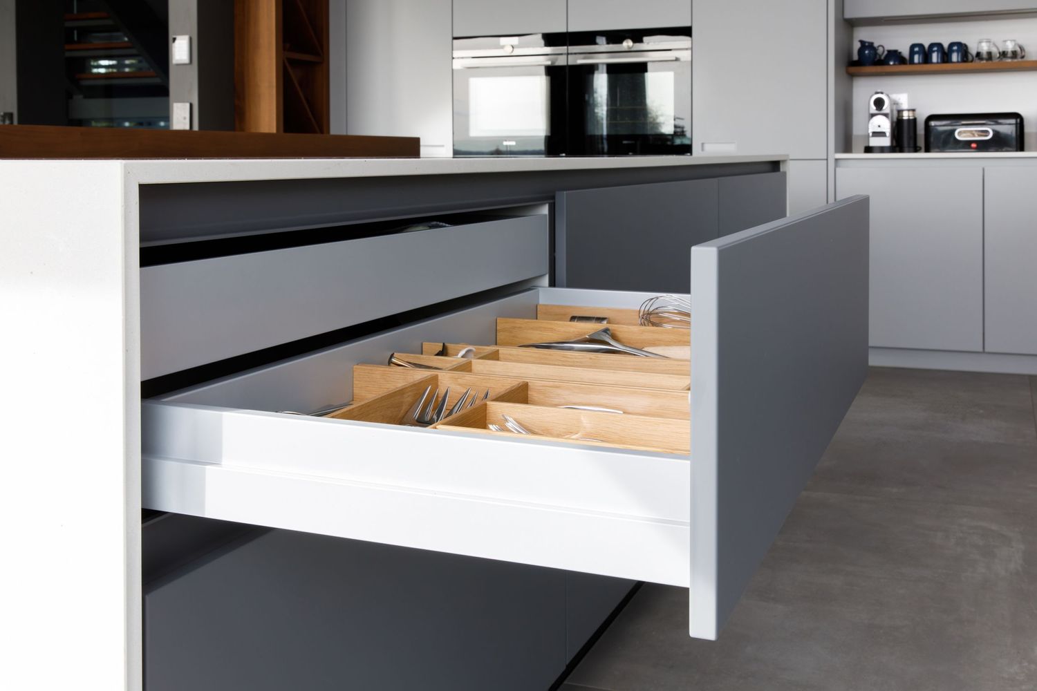 Pull-out kitchen drawer showing wooden cutlery organizer inside grey cabinet with handleless design taken during an kitchen photoshoot.
