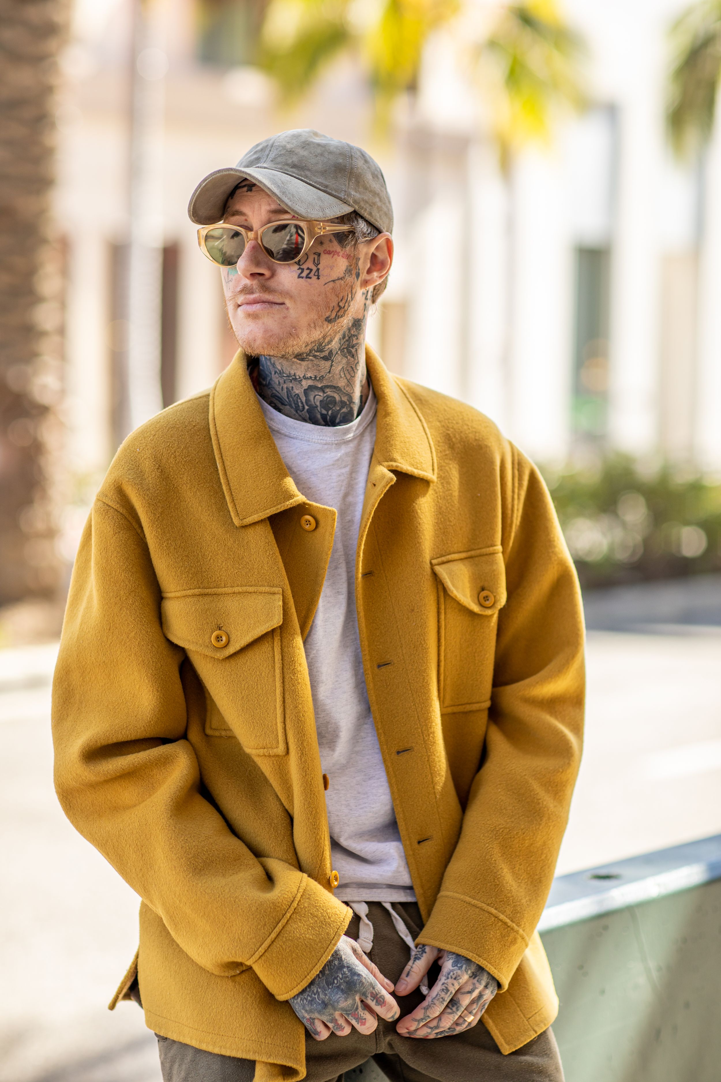 Street style portrait in mustard jacket, baseball cap and sunglasses.
