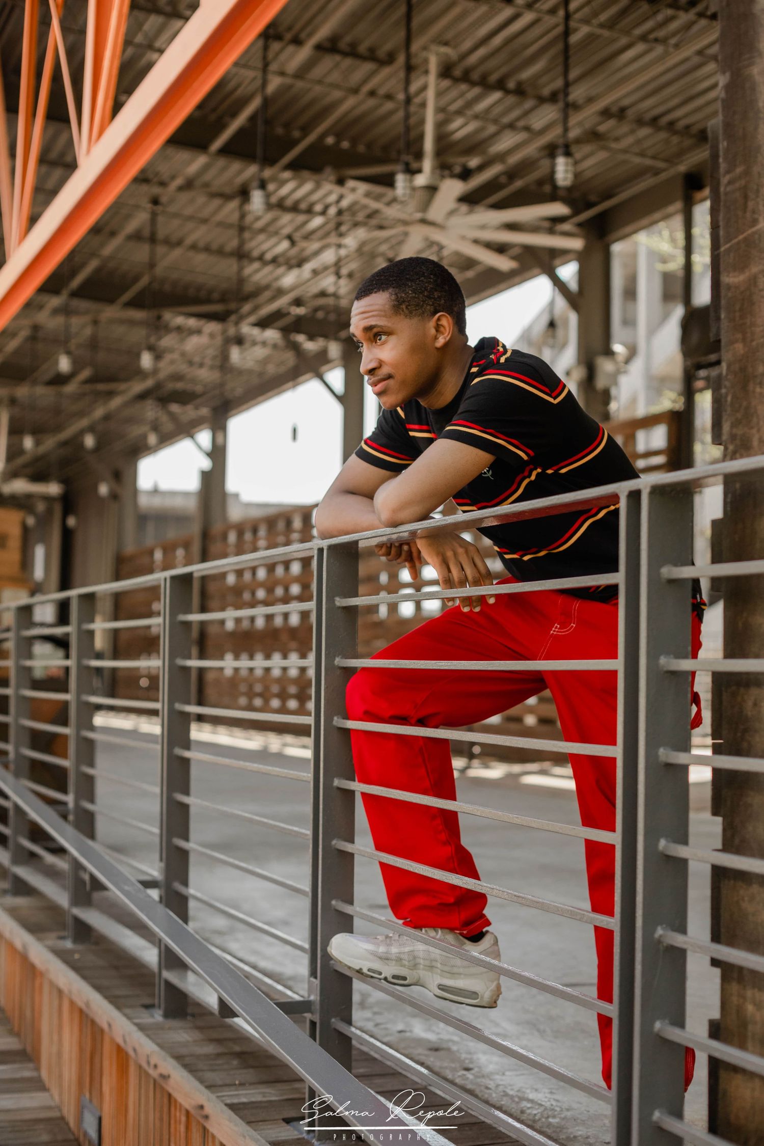 Person in red and black outfit leans on railing in industrial setting.