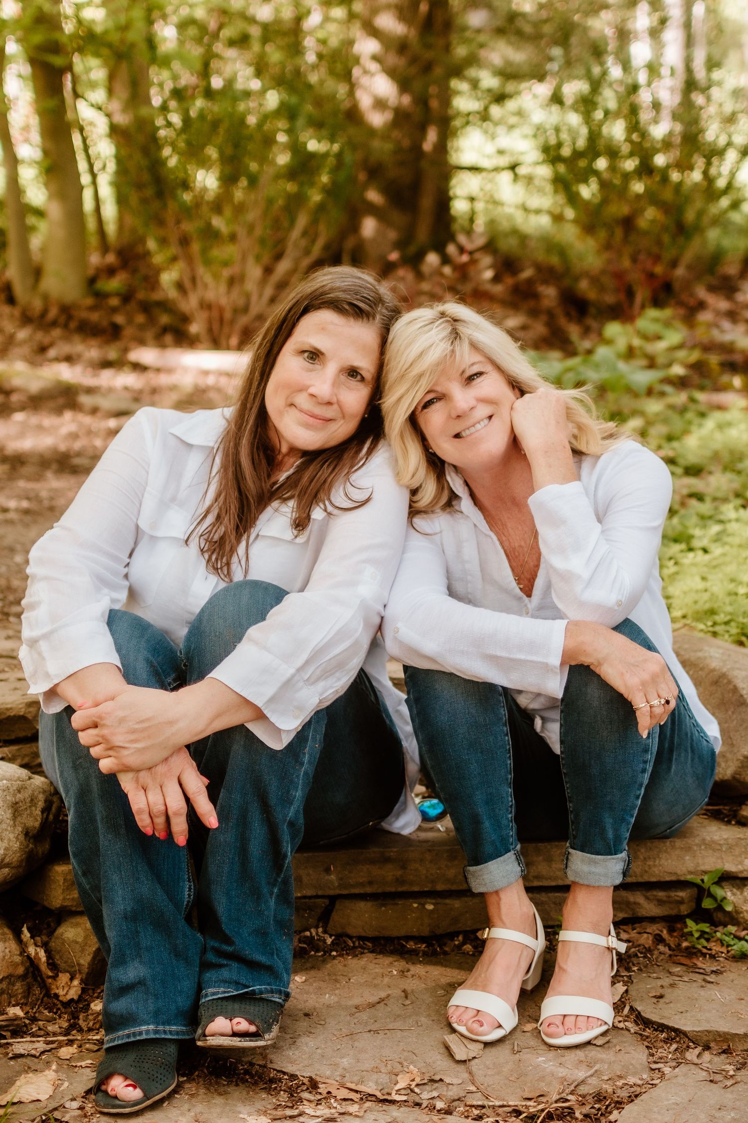 Two people in white shirts and jeans sitting casually on wooden steps outdoors.