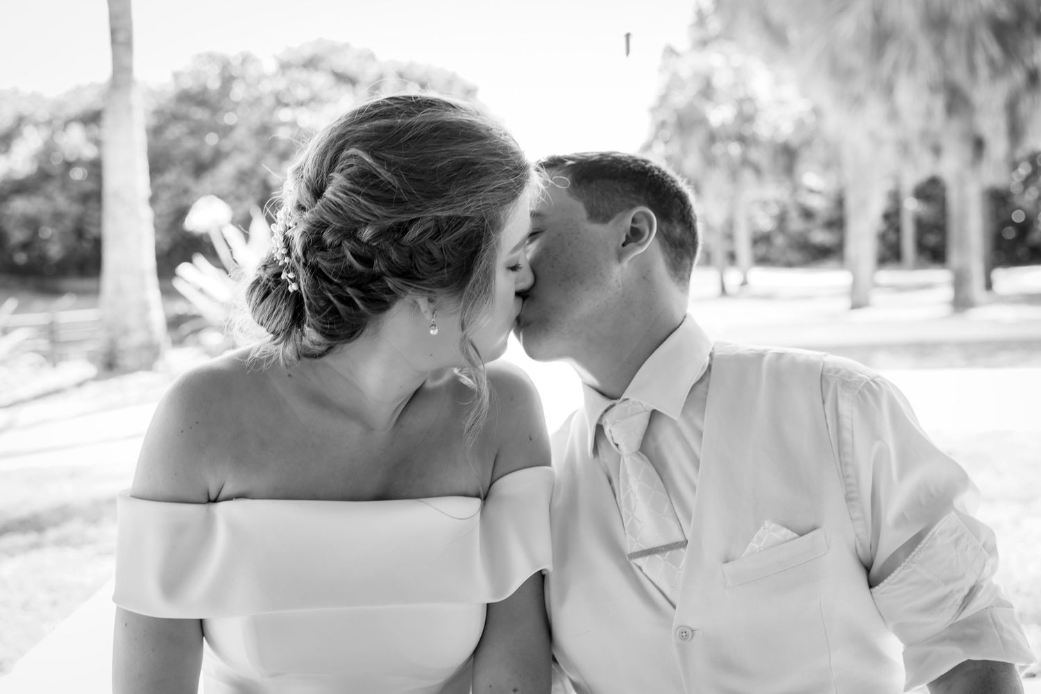 Black and white photo of bride and groom kissing at outdoor wedding ceremony.