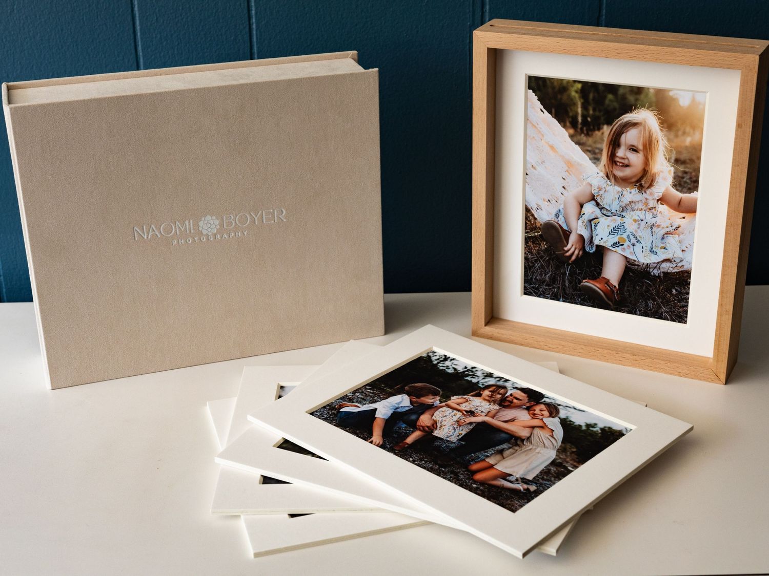 A collection of printed photos and an elegant photo album displayed on a blue background.