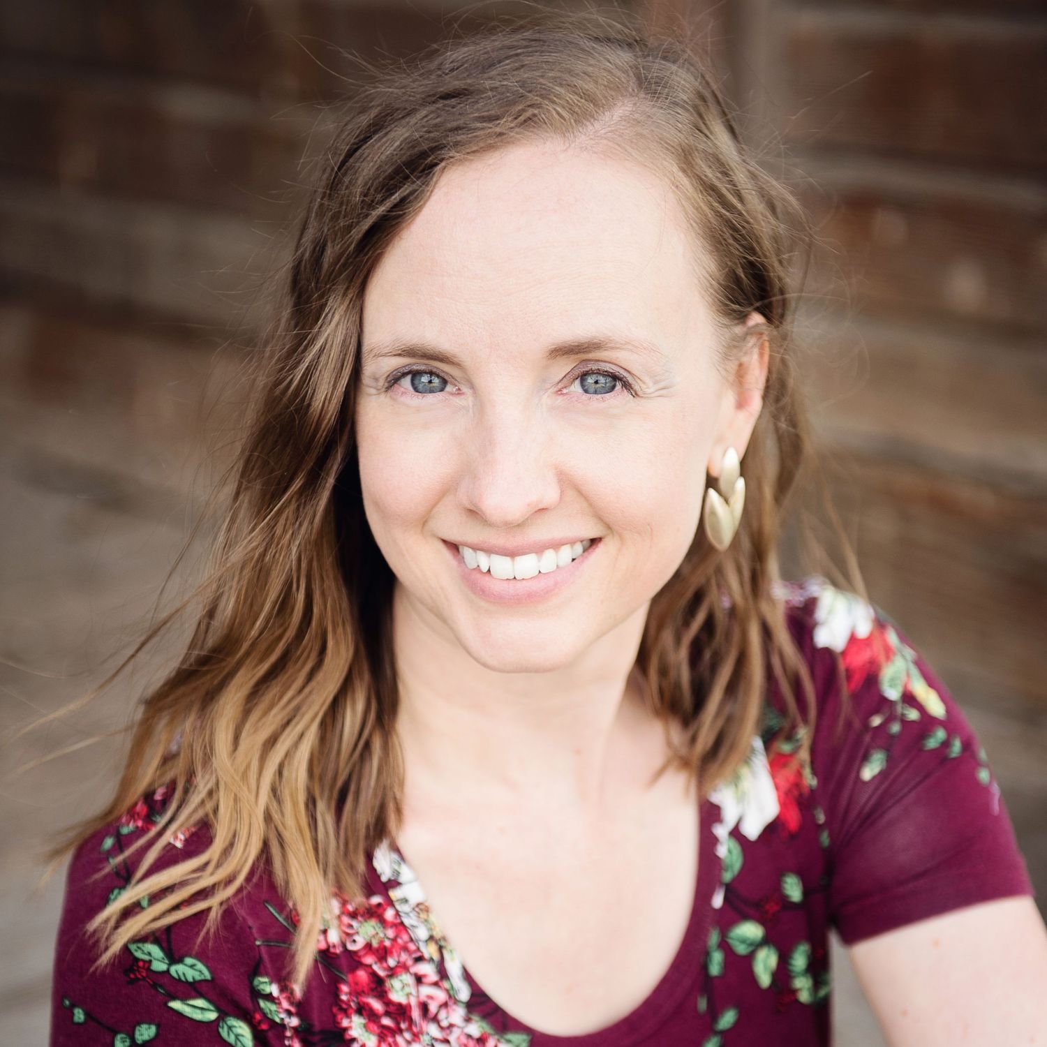 Professional headshot portrait against brick wall background with burgundy floral top.