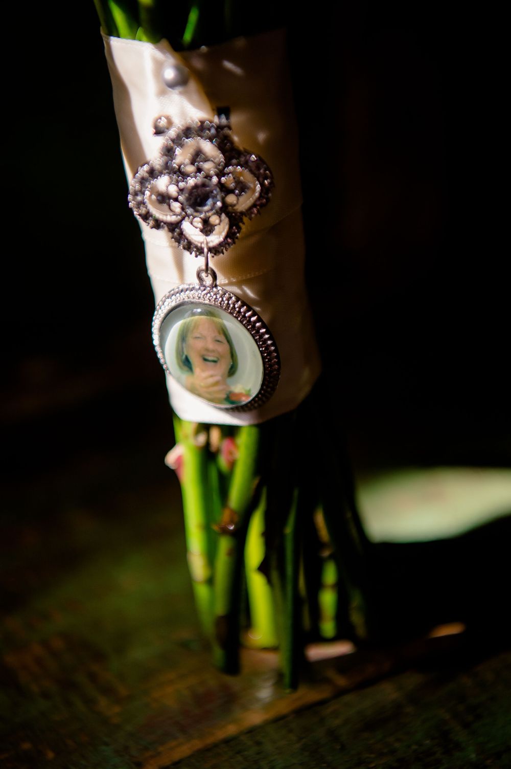Ornate vintage locket with photo charm attached to a bouquet stem in dramatic lighting.