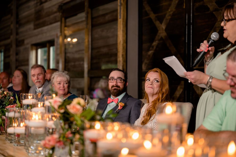 Reception dinner scene with candlelit tables in rustic wooden venue during wedding celebration.