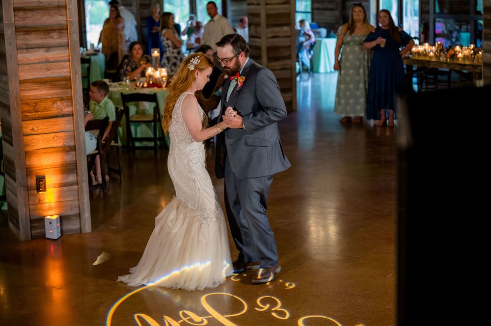 Newlyweds share first dance on illuminated wooden floor during reception.