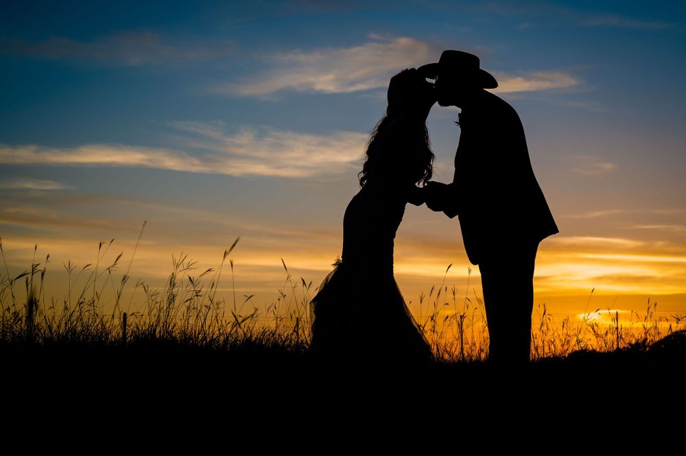 Silhouette of a couple in western wedding attire embracing against a dramatic sunset sky.