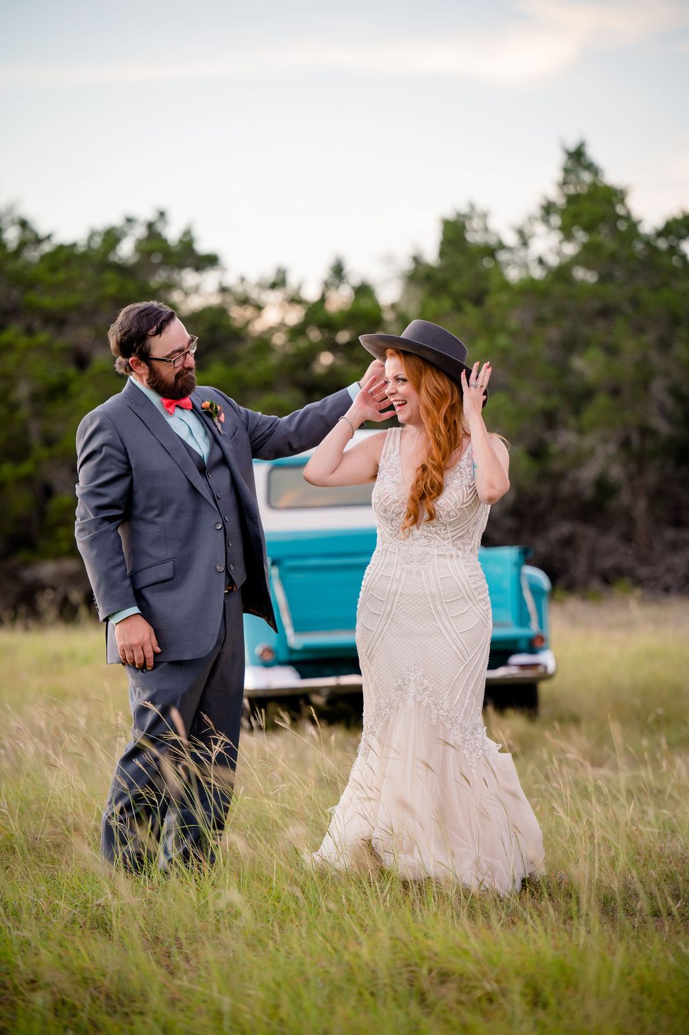 A joyful wedding moment captured near a vintage blue car in a rustic field setting.