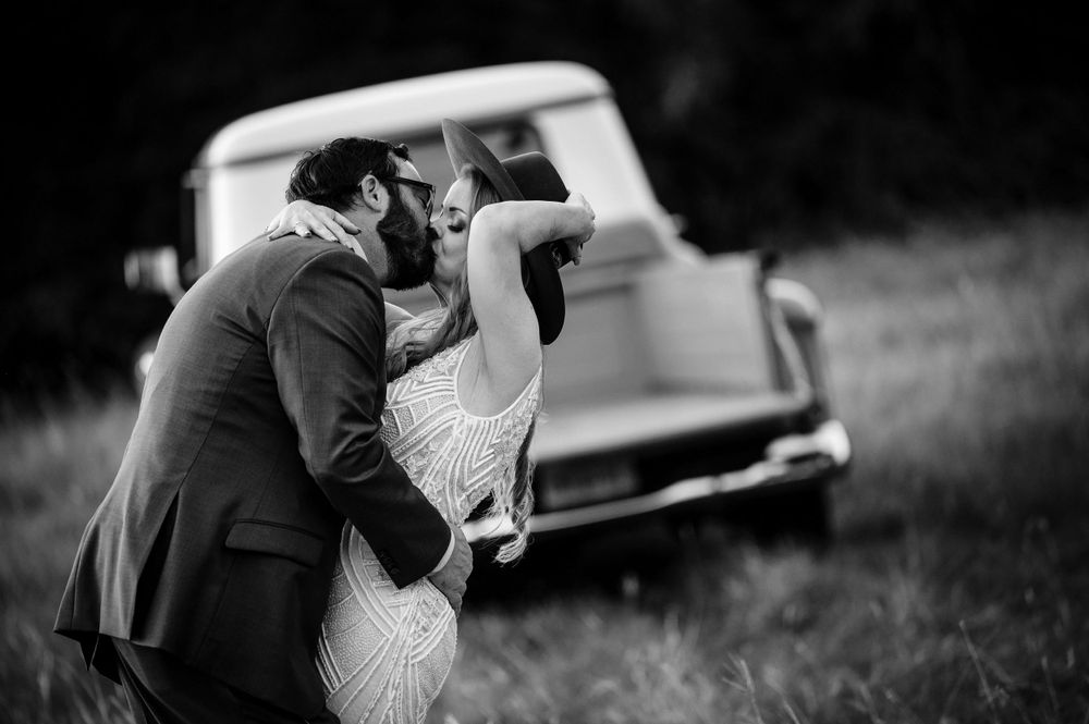 Black and white wedding photo of a romantic embrace with a classic truck in the background.