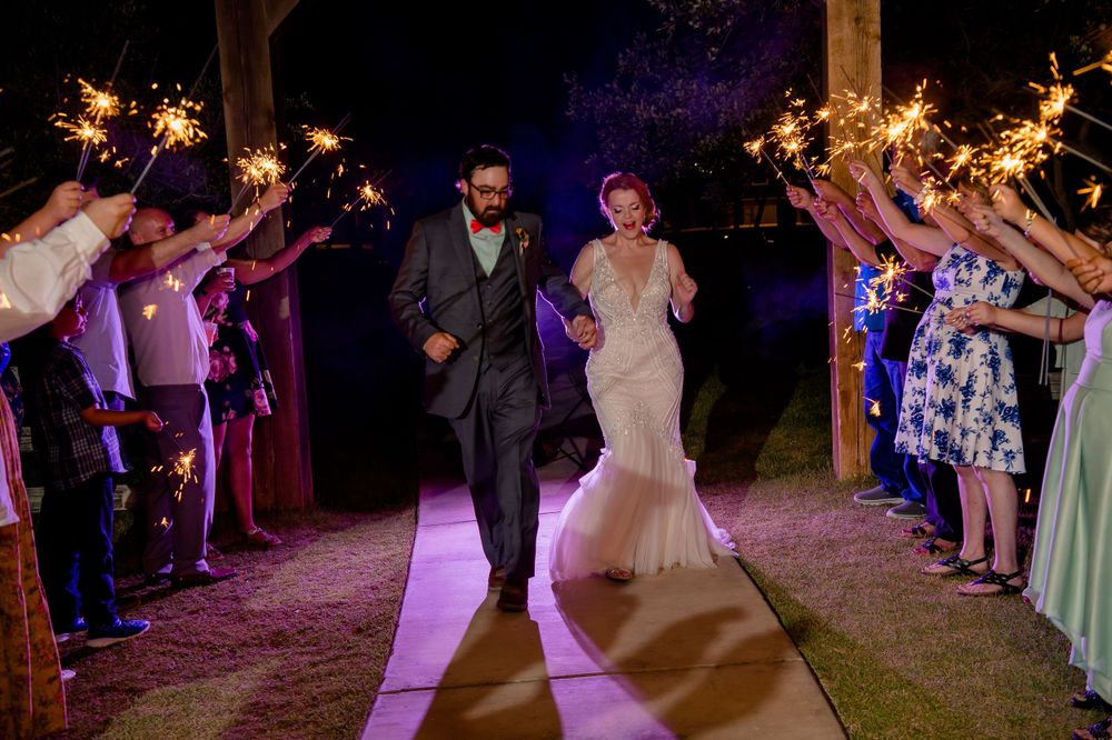 Wedding couple exits through sparkler tunnel held by guests during nighttime celebration.