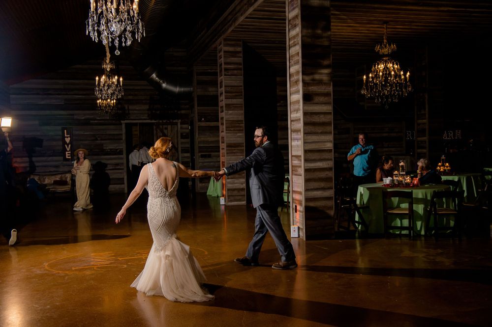 Wedding dance in rustic venue with wooden beams and elegant chandeliers.