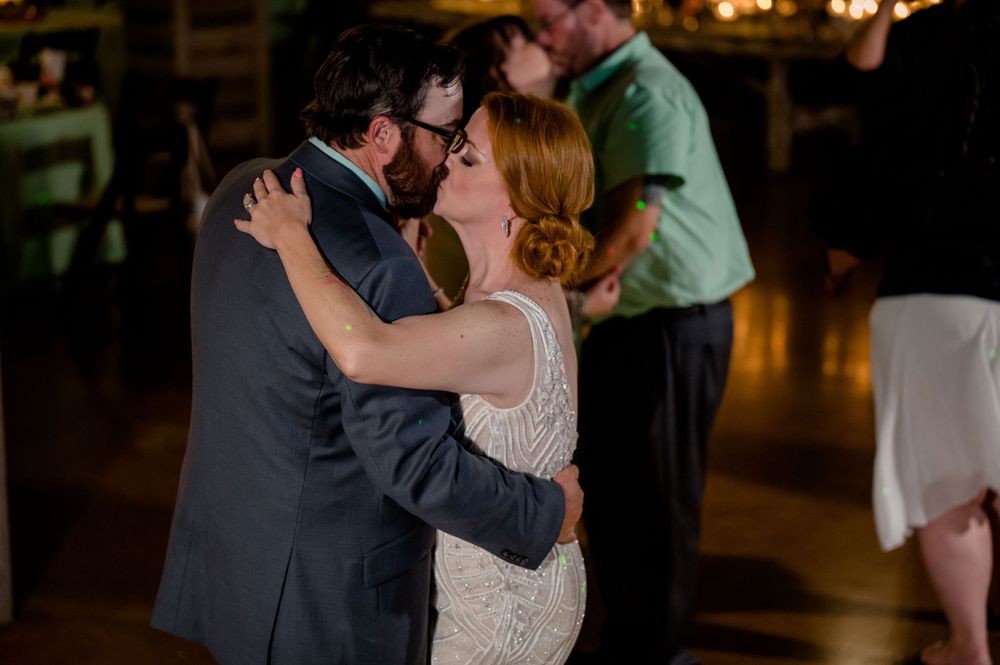 Intimate slow dance moment during wedding reception in rustic wooden venue.