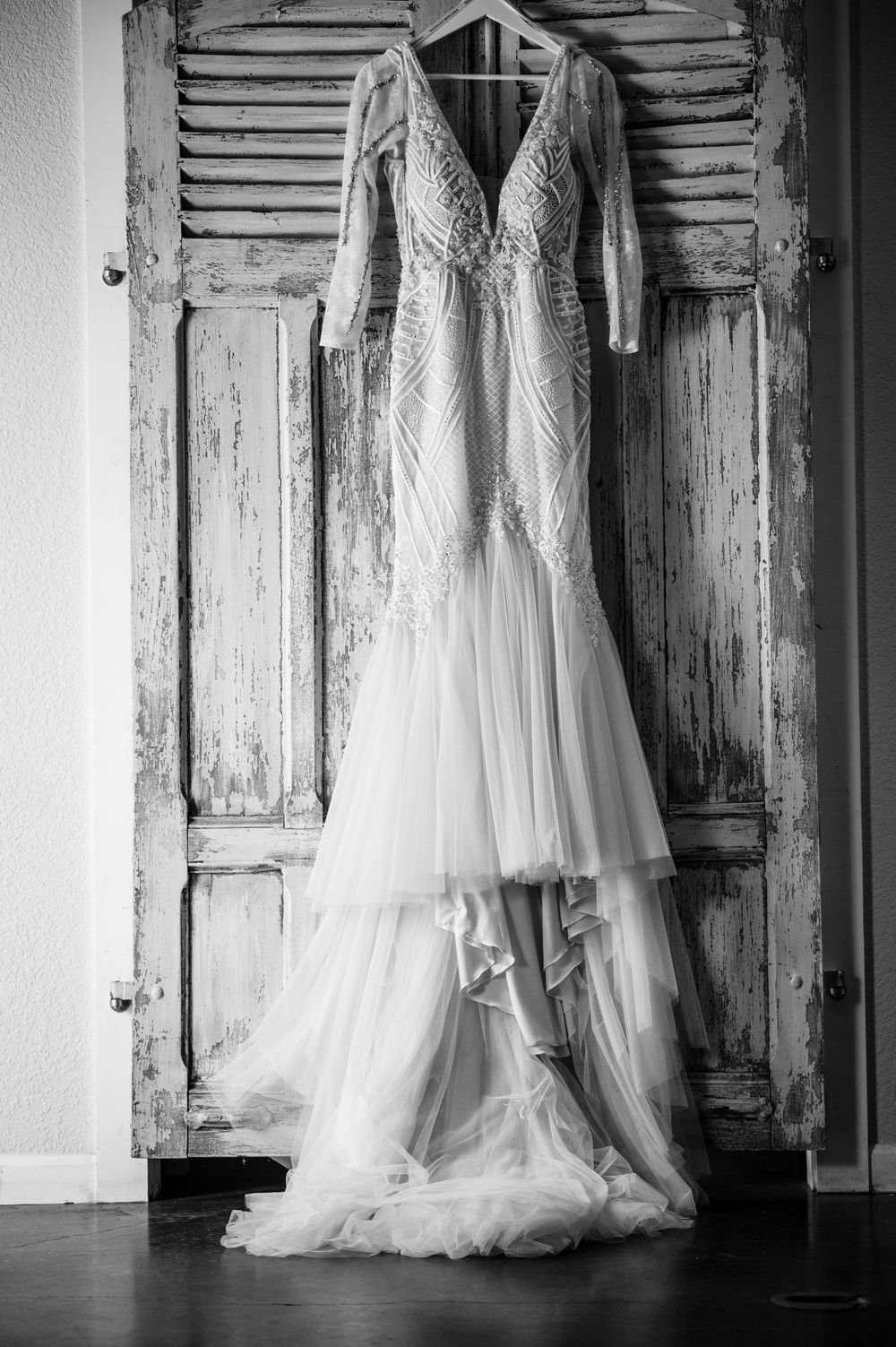 White lace wedding dress with flowing train hanging on rustic wooden doors in black and white.