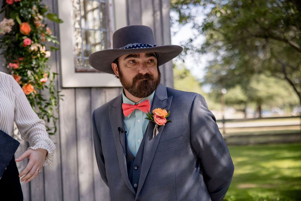 Wedding portrait of groom in grey suit with coral bow tie and western hat.