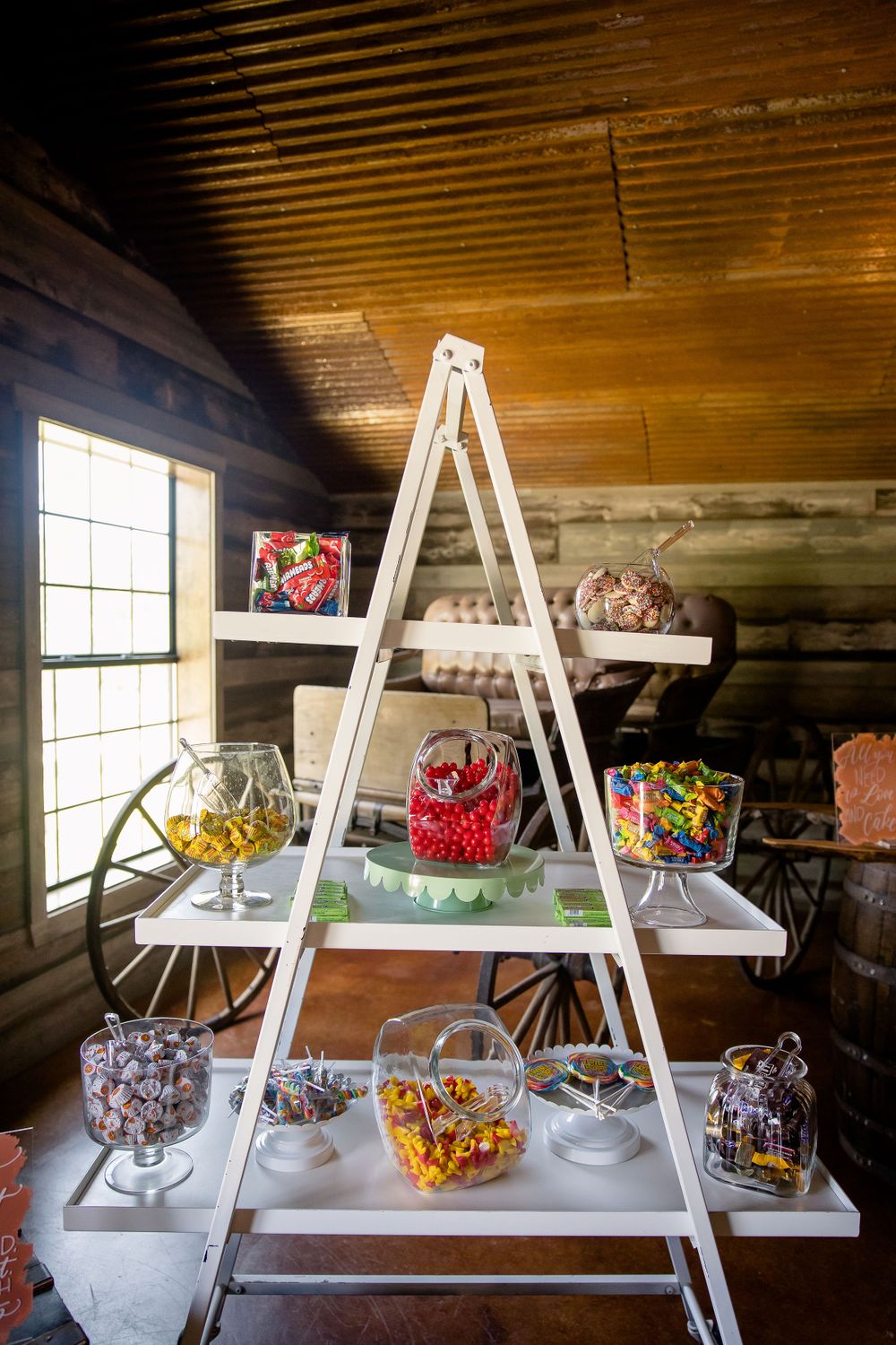 White ladder shelf displaying colorful candy jars at a rustic wedding reception.