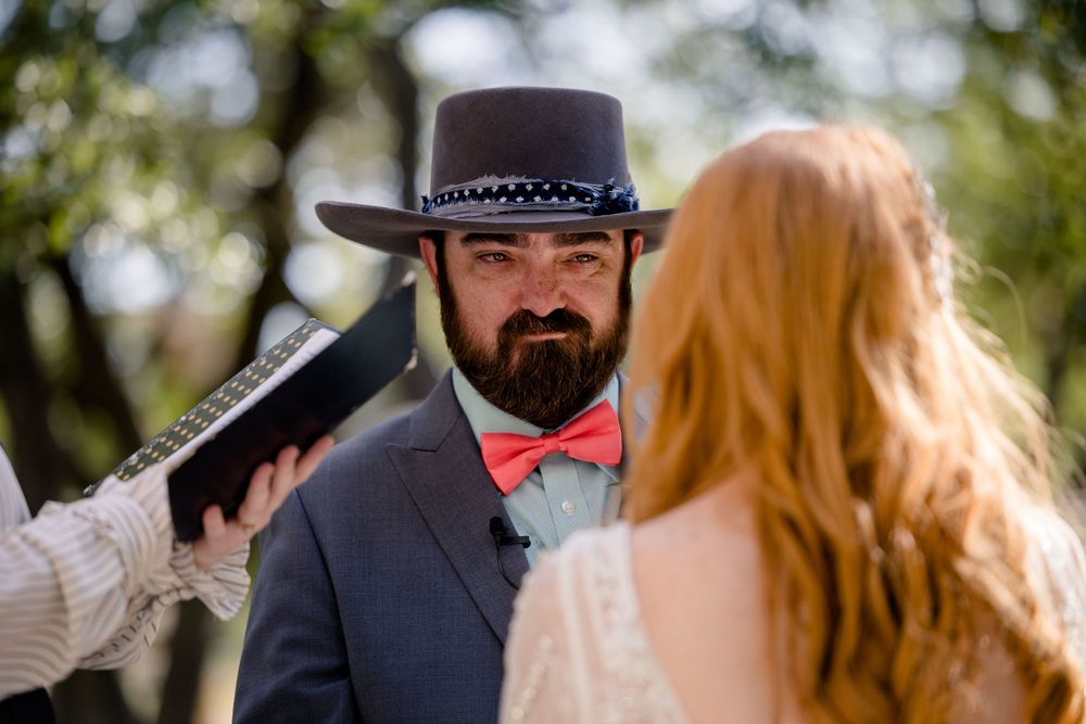 A wedding ceremony in progress showing a man in a suit and hat with red bowtie during the vows.