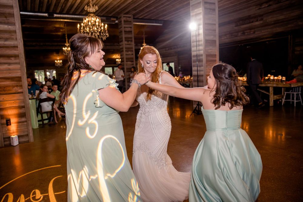 Wedding guests dance together under elegant chandeliers in a rustic wooden reception venue.