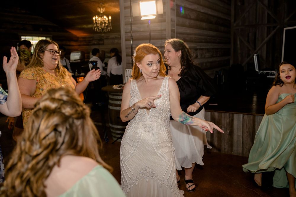 Joyful celebration on the dance floor at a rustic wedding reception with wooden walls and warm lighting.