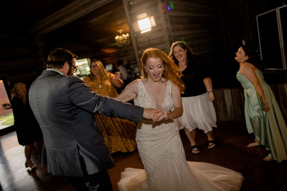 Wedding celebration with dancing under elegant chandeliers in a rustic wooden venue.