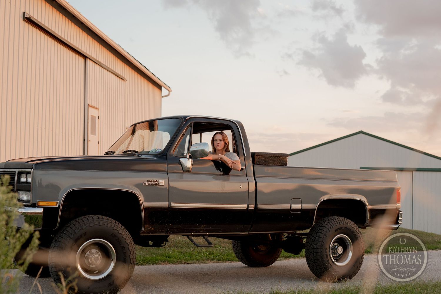 Lifted classic Chevrolet pickup truck parked outside industrial buildings at dusk.