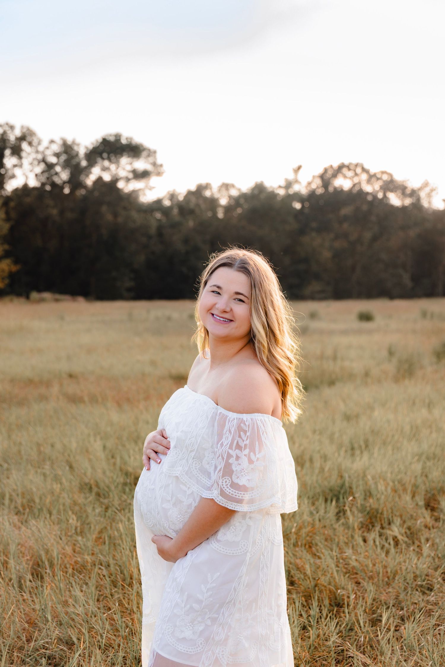 Woman in white lace dress twirling in sunlit field.