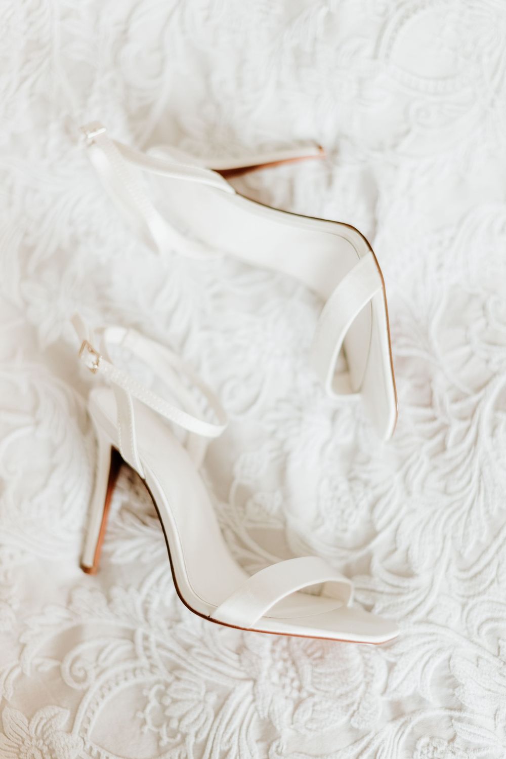 Elegant white bridal heel sandals on lace background.