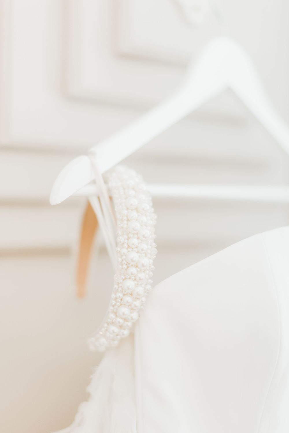 White pearl buttons line the back of an elegant wedding dress hanging on a white hanger.
