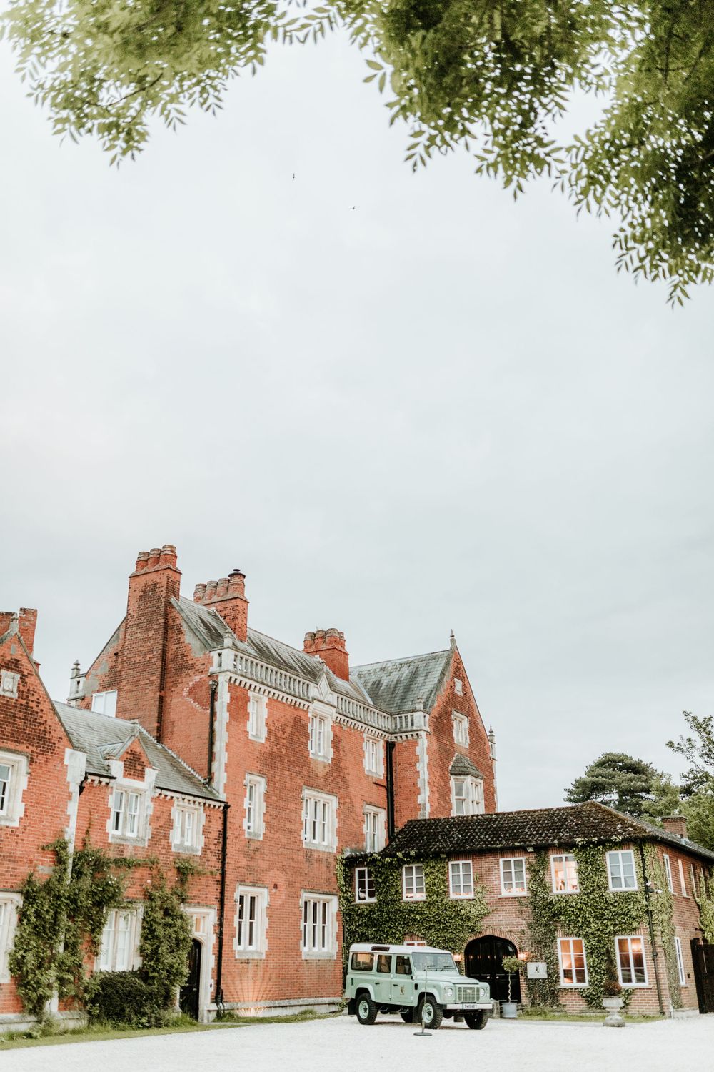 Red brick manor house with vintage Land Rover parked under archway.