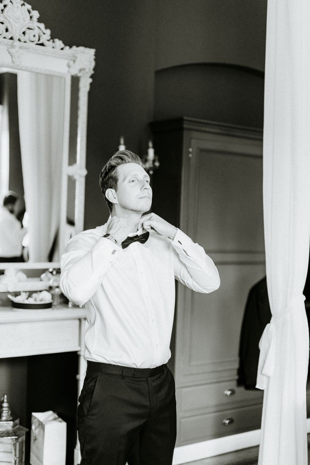 Black and white photo of person adjusting bowtie in formal wear.