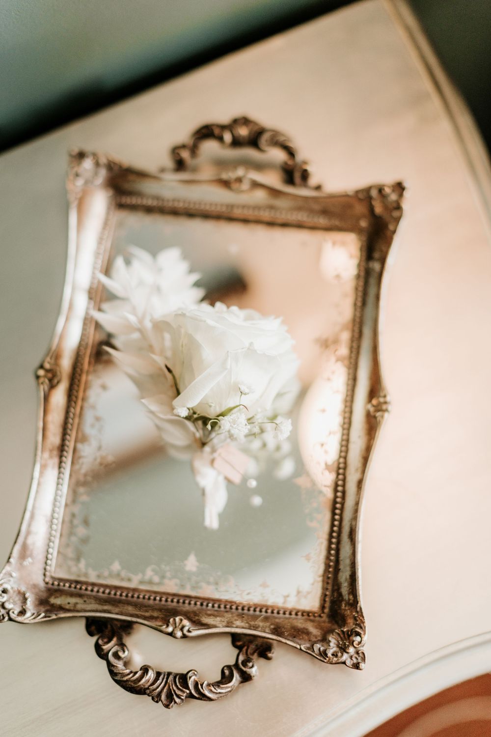 White flowers displayed in an ornate vintage gold frame mirror on light surface.
