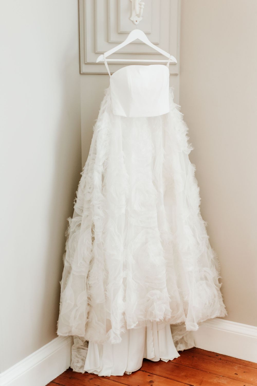 White wedding dress with textured skirt hanging on display.