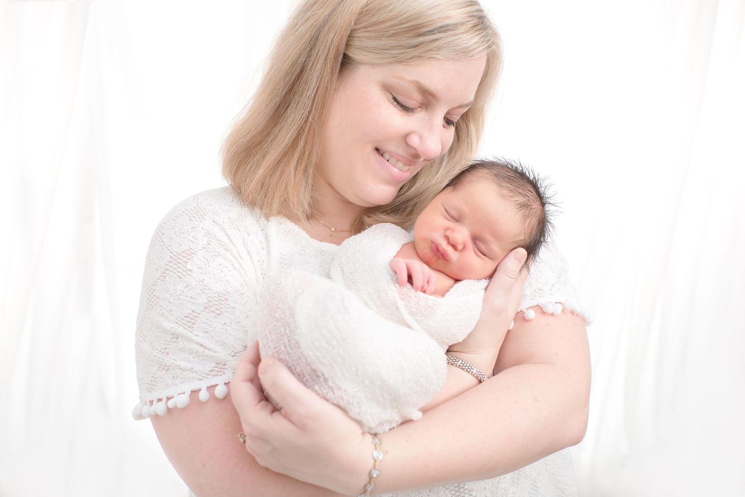 mom smiling at her newborn four day old baby boy in an all white wrap in houston texas