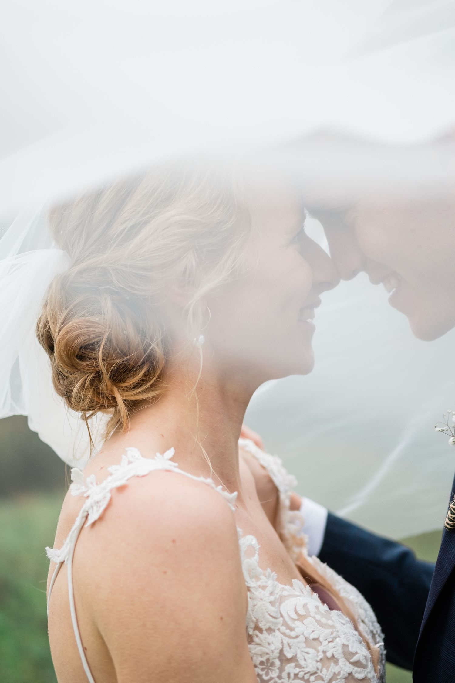 Romantic soft-focus portrait of couple under a wedding veil in natural light.