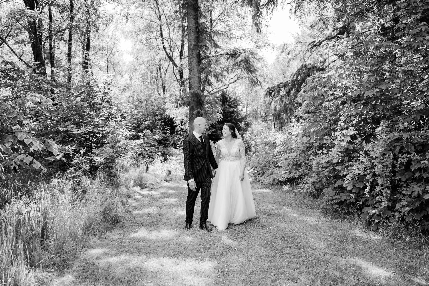 A couple takes a romantic stroll through a wooded path in black and white.