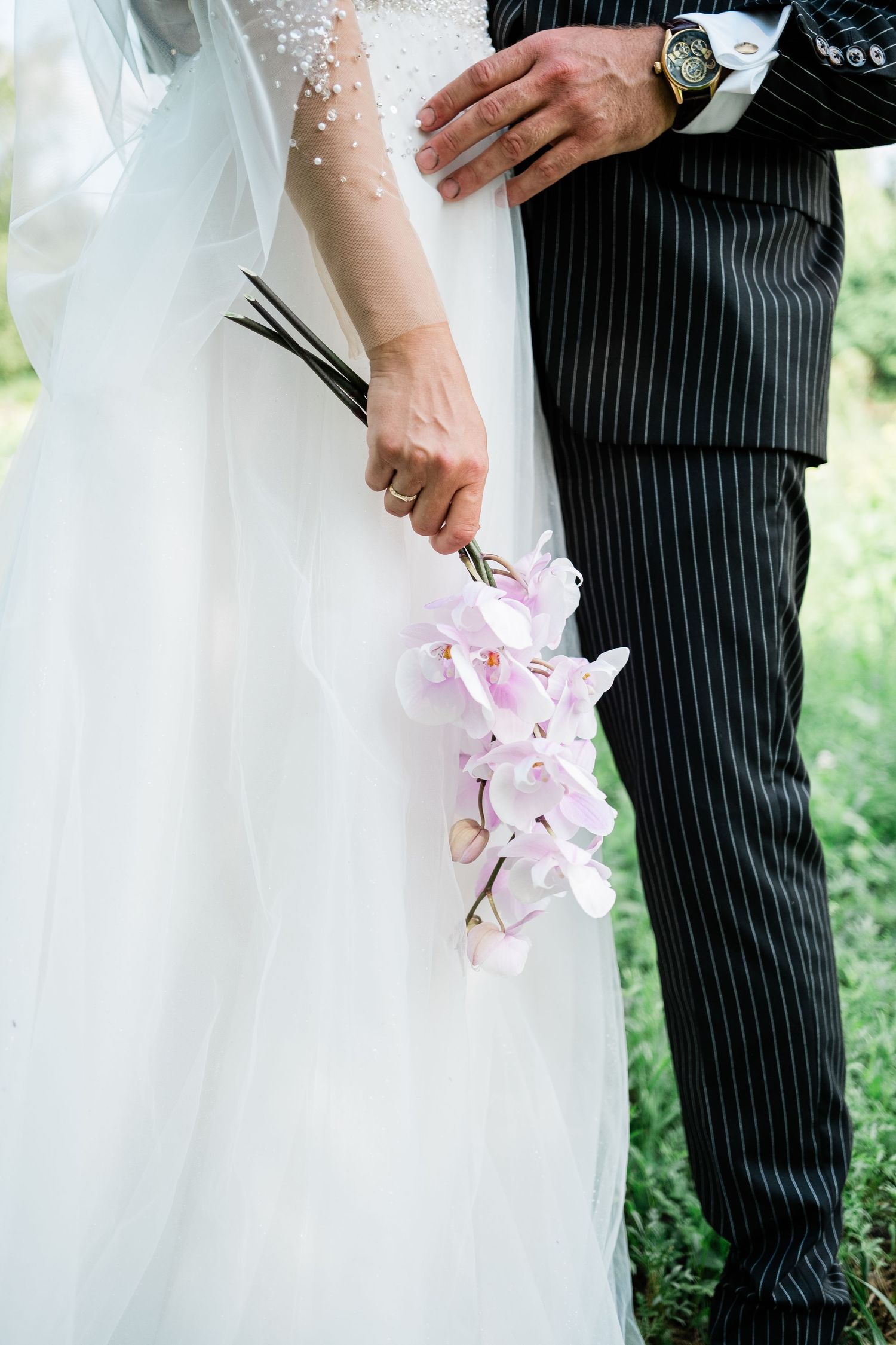 Close-up of bride's delicate pink orchid bouquet next to groom's pinstriped suit.