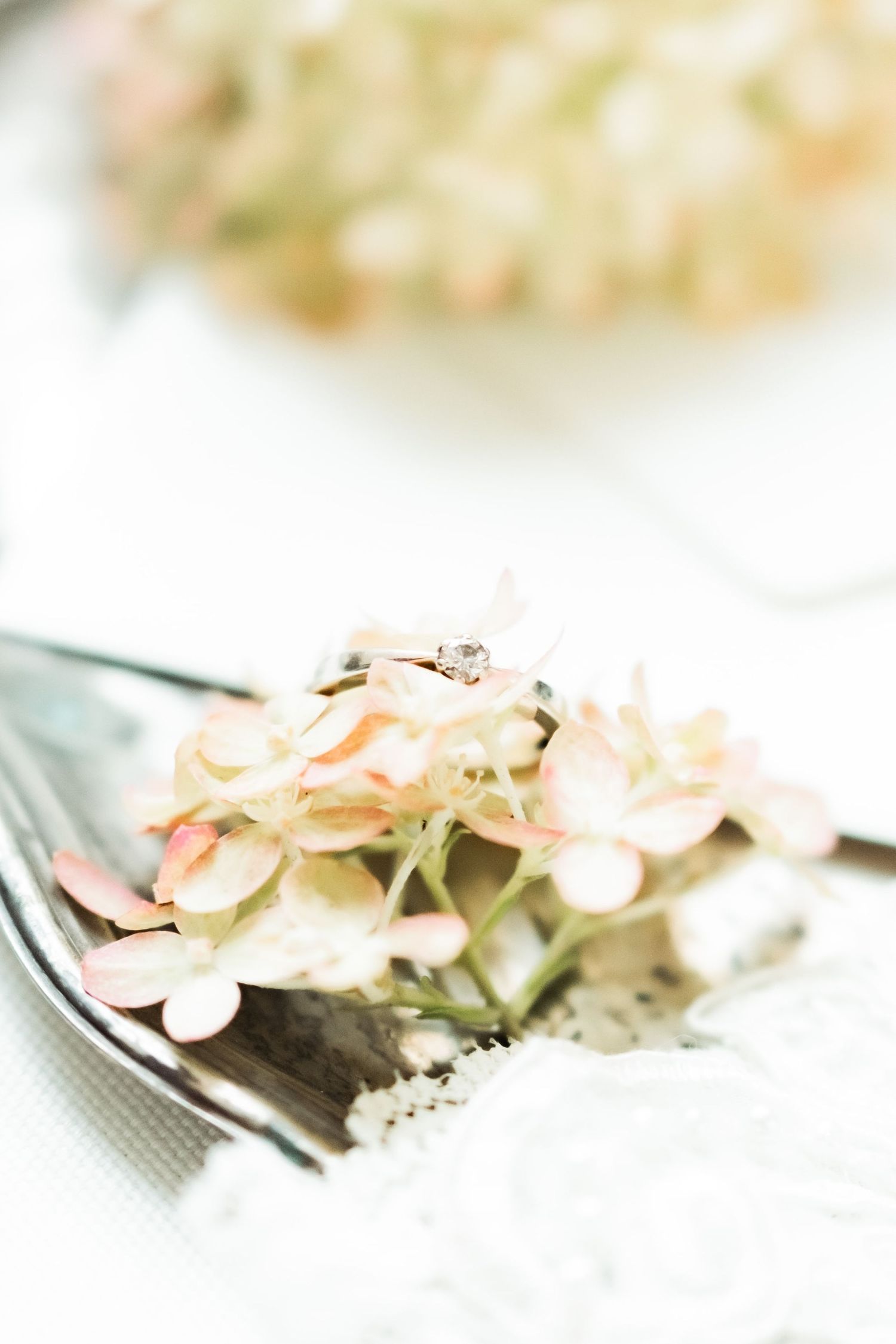 A wedding ring nestled among soft pink hydrangea petals on a silver fork.