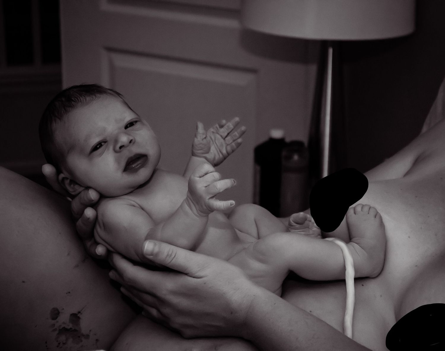 Black and white image of a newborn baby looking straight at the camera while being held by her mother.