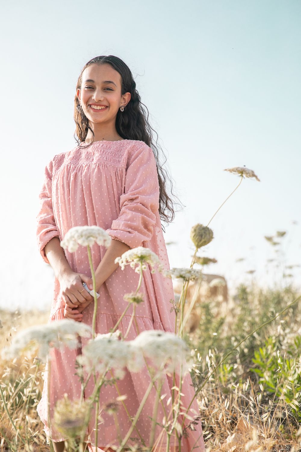 A girl standing in a golden field and white flowers in front