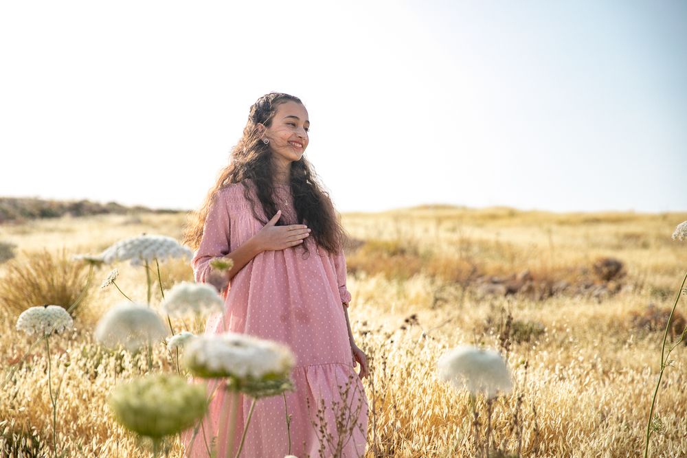 A girl standing in a golden field and white flowers in front